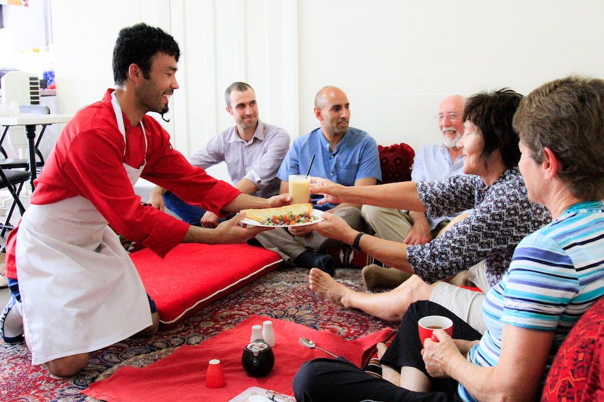 People sit on pillows and rugs as they are served food in a takeaway shop