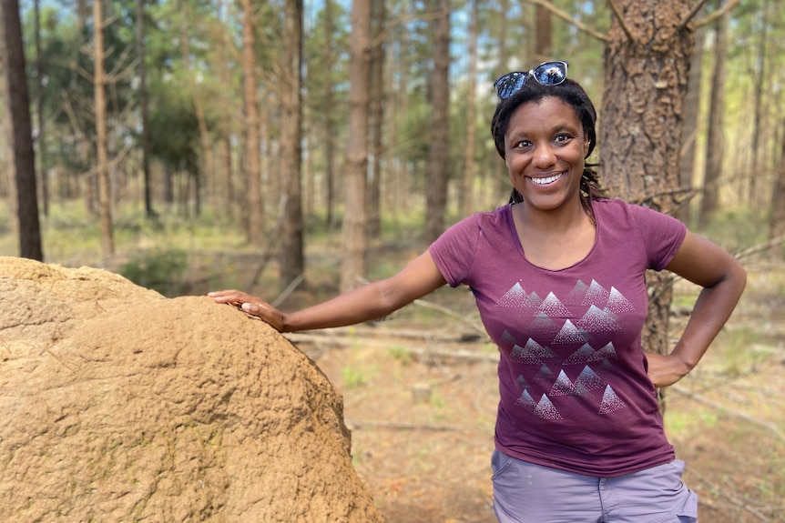 woman in pruple t-shirt leaning against large rock in the bush