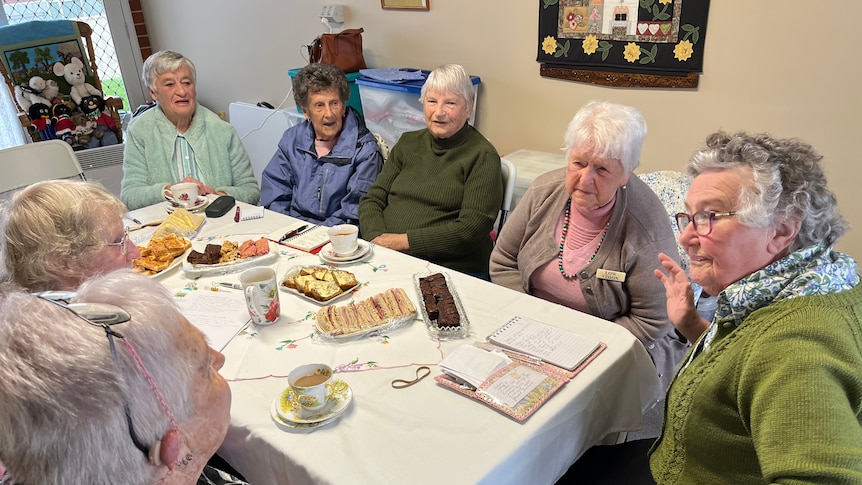 A group of older ladies sit around a table eating afternoon tea 