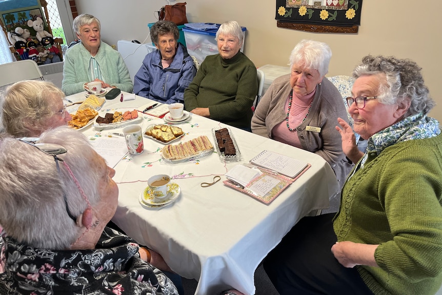 A group of older ladies sit around a table eating afternoon tea 