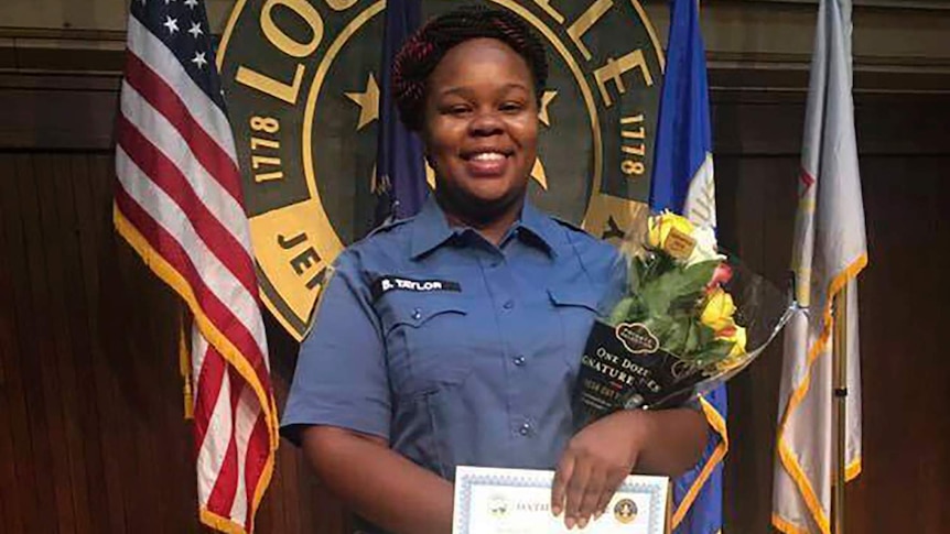 Breonna Taylor smiles in a uniform holding a certificate and flowers.