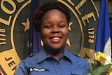 Breonna Taylor smiles in a uniform holding a certificate and flowers.