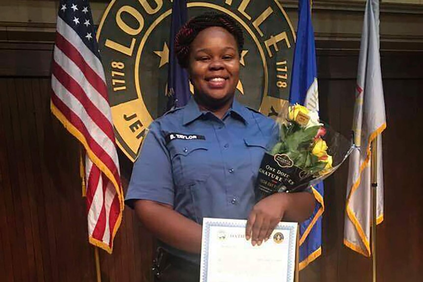 Breonna Taylor smiles in a uniform holding a certificate and flowers.
