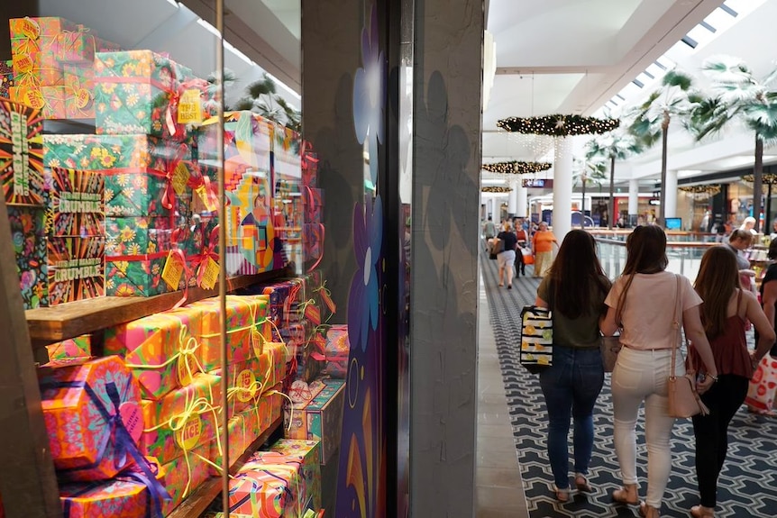 Christmas shoppers at Carindale shopping centre walk past a shop display of presents