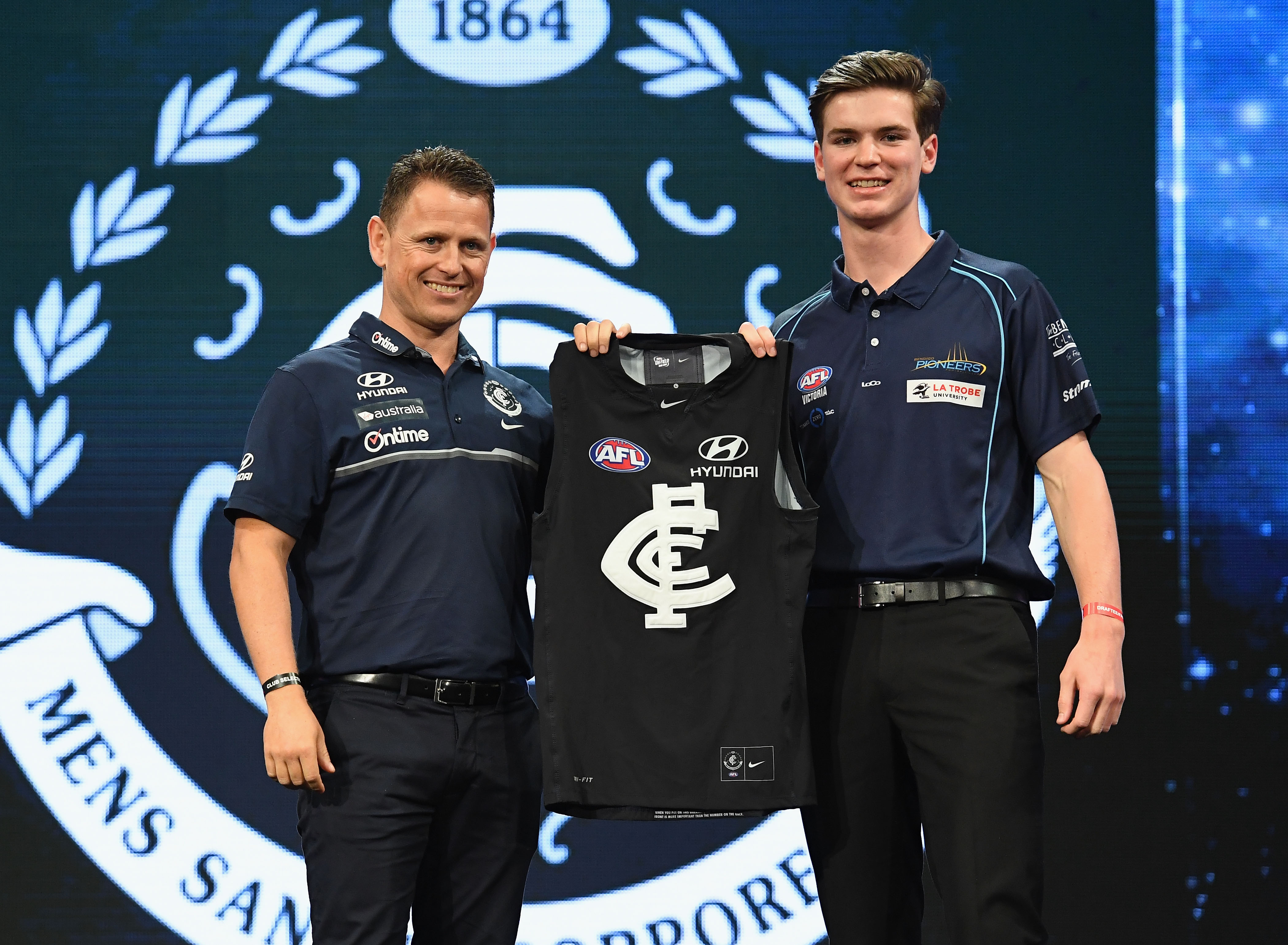 Paddy Dow holds up a Carlton jersey with Brendon Bolton
