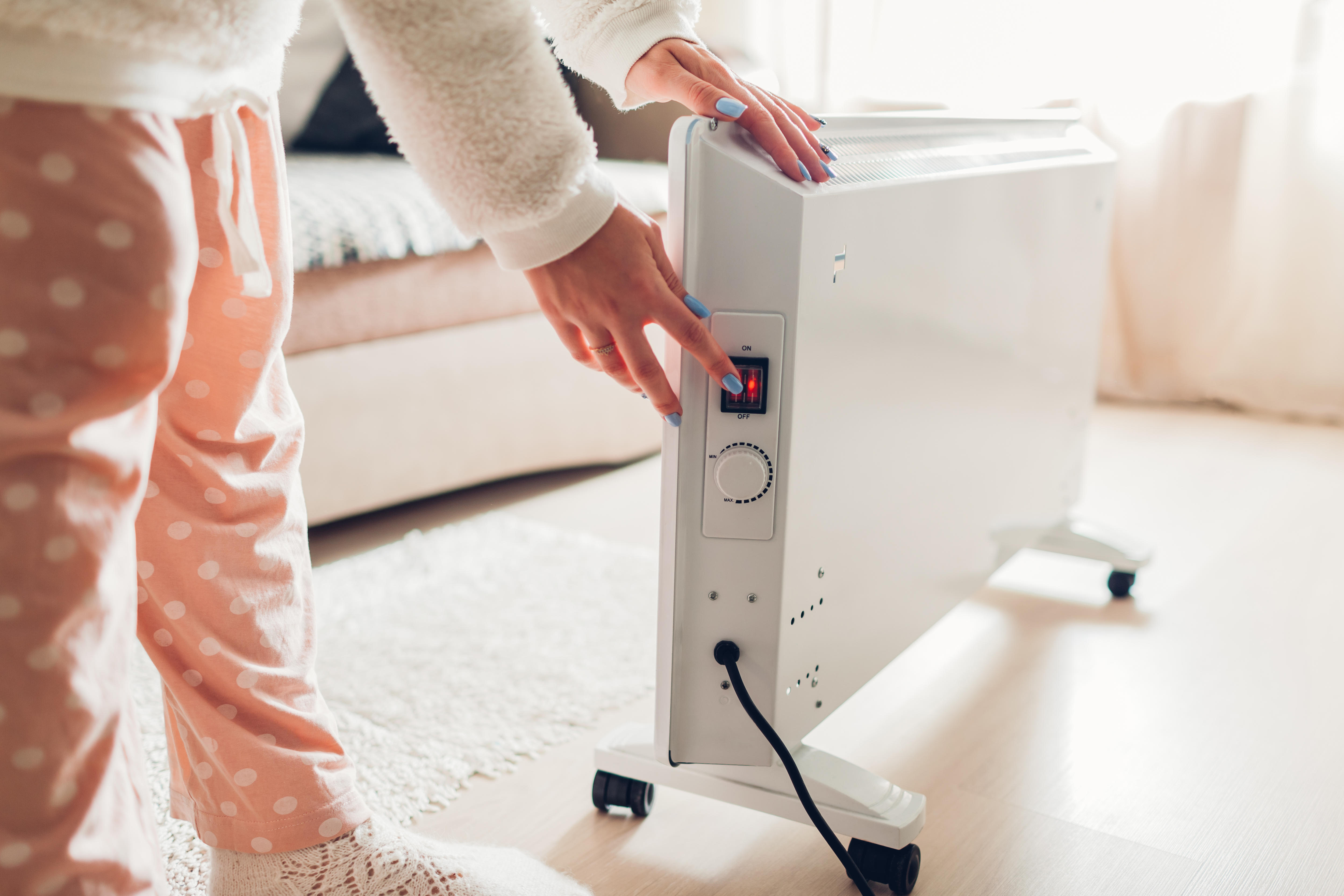 A woman turns a switch on an electric heater.