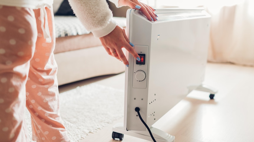 A woman turns a switch on an electric heater.