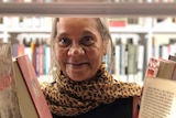 Ms Moreton smiles at camera, through a gap of books in the aisle of a library.
