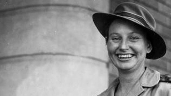 A woman in military uniform smiles at the camera while holding a bunch of flowers.