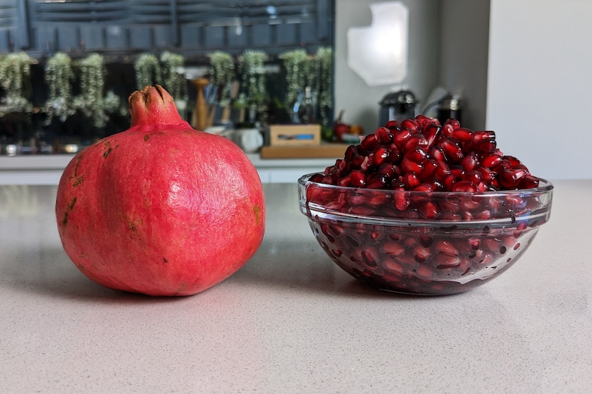 A ripe pomegranate next to a glass bowl of arils.