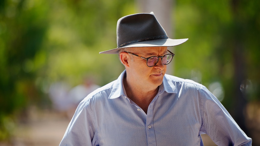 Australian Prime Minister Anthony Albanese in a blue collared shirt and Akubra hat, standing outside and looking down.