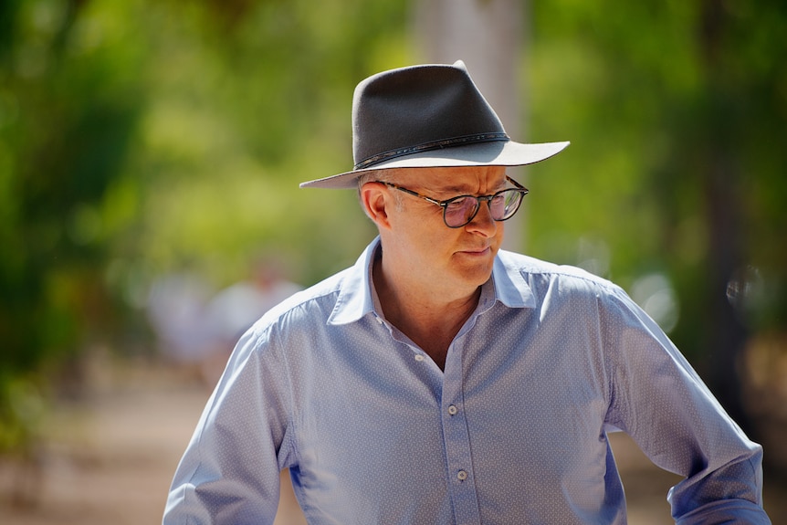 Australian Prime Minister Anthony Albanese in a blue collared shirt and Akubra hat, standing outside and looking down.