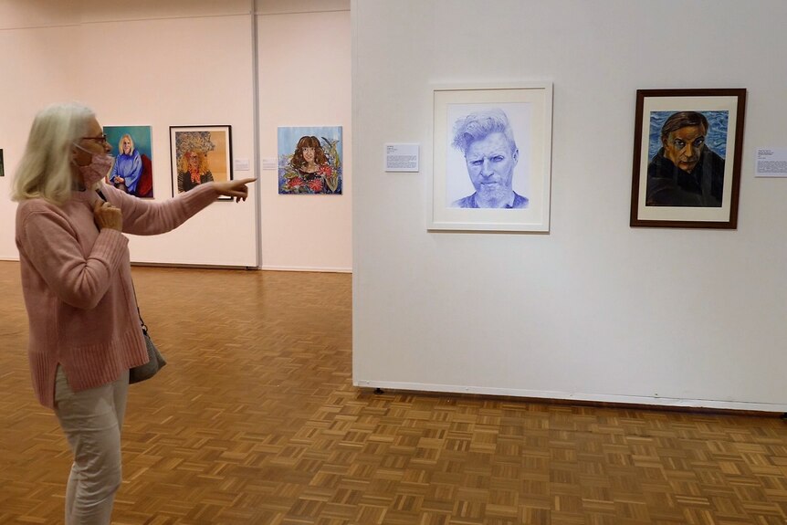 A woman points at a detailed portrait of a young man drawn in blue biro