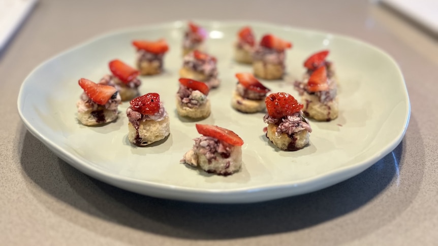 Canapes consisting of smoked chicken on brioche rounds with pickled strawberries and red wine reduction on a large white plate.