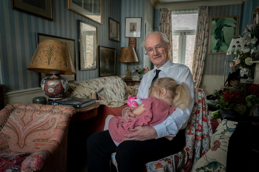 A father cradles his young daughter in a living room.