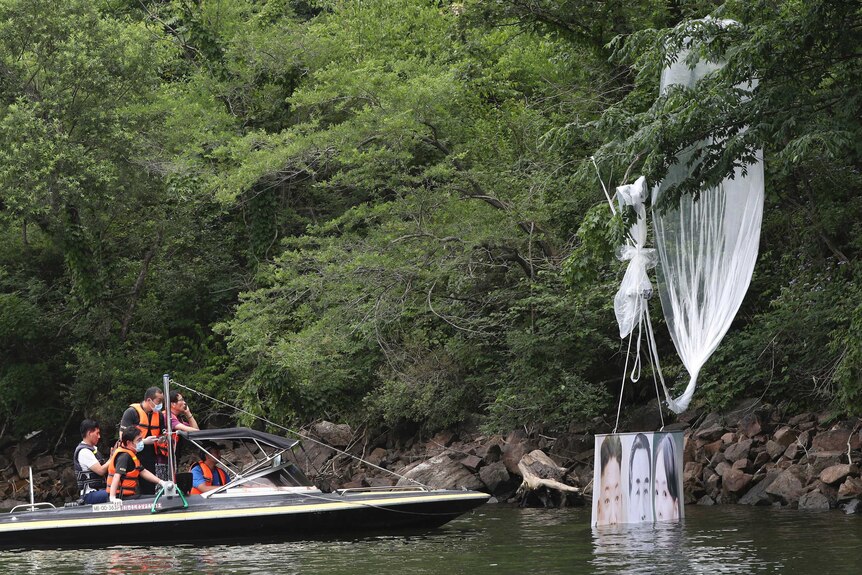 Men in a boat sail towards a balloon hanging in a tree, the balloon has a picture of past and current North Korean leaders.