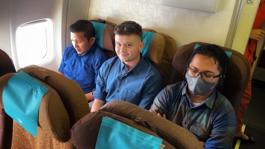 Bodhi Risby-Jones smiles at the camera while sitting in an plane next to two men