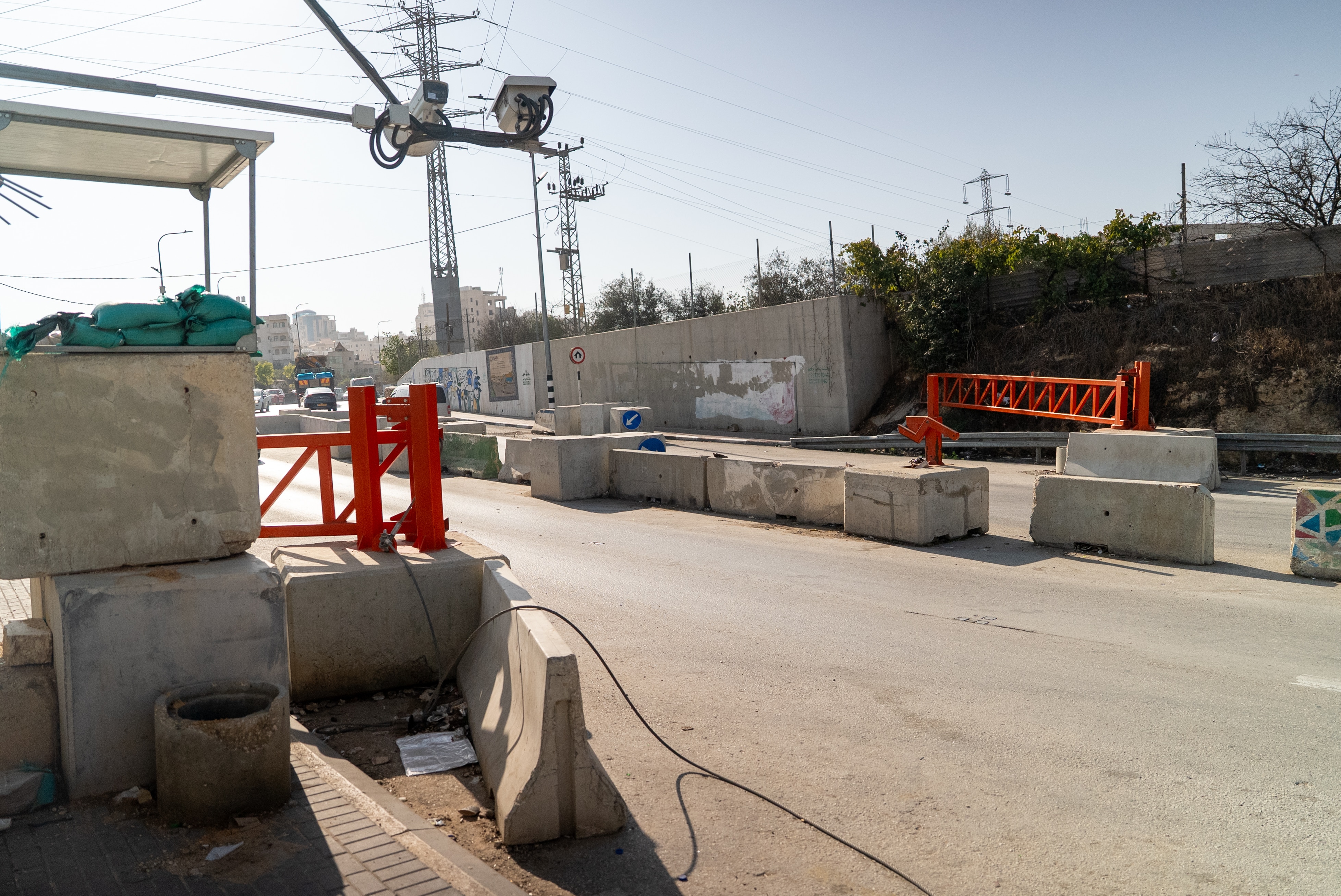 A road with barriers on the side and open gates, guard station and cameras on poles above
