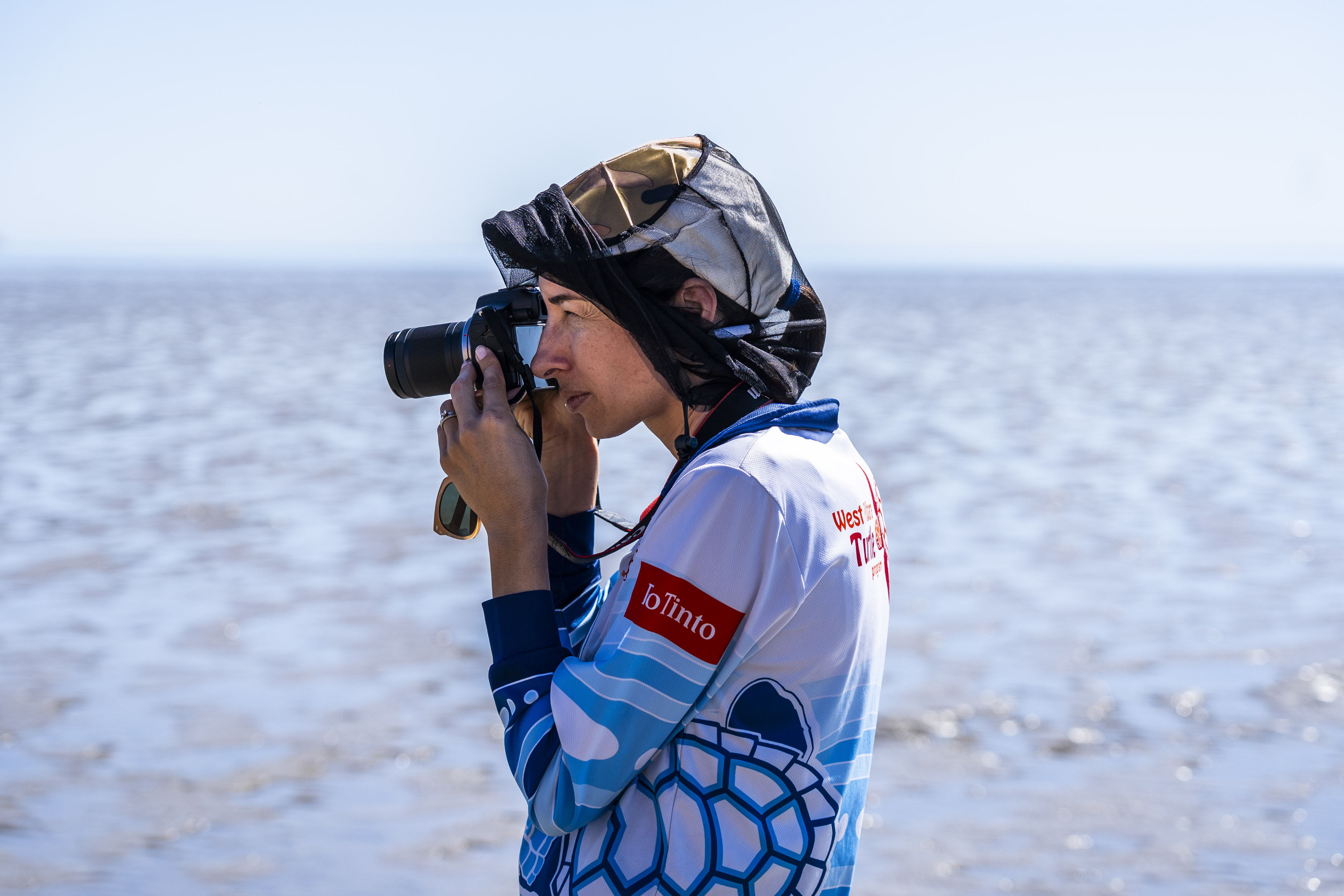 Uma mulher com binóculos olha de soslaio para o céu e a água.