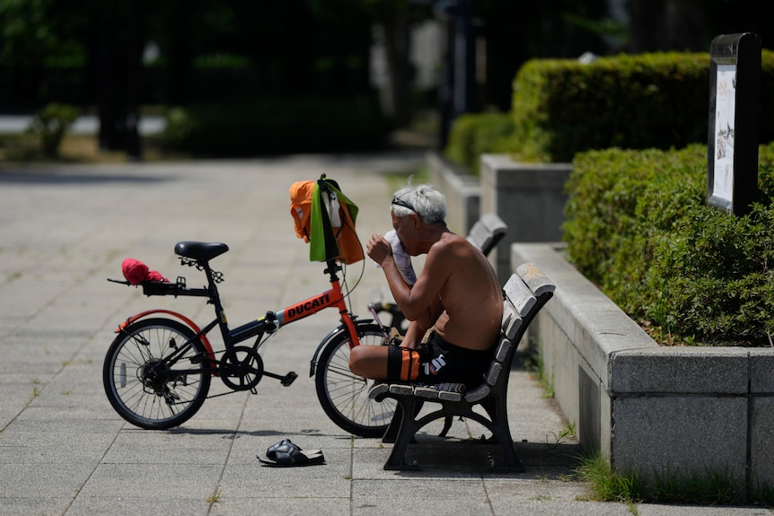 A cyclist wipes sweat off his face as he takes a break at a park 