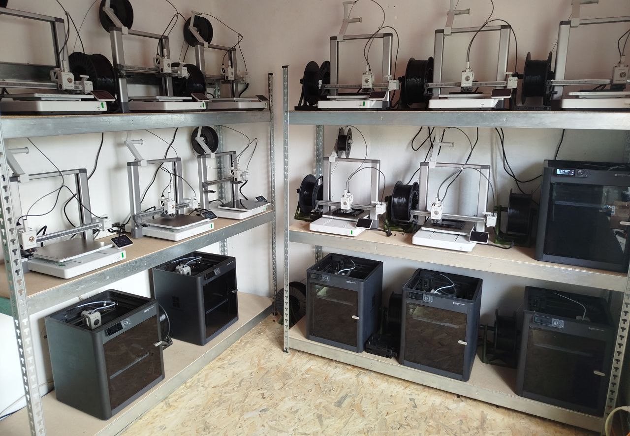 3D printers on shelves cover the walls of a small room