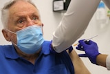 Elderly man in blue shirt, blue mask gets vaccination