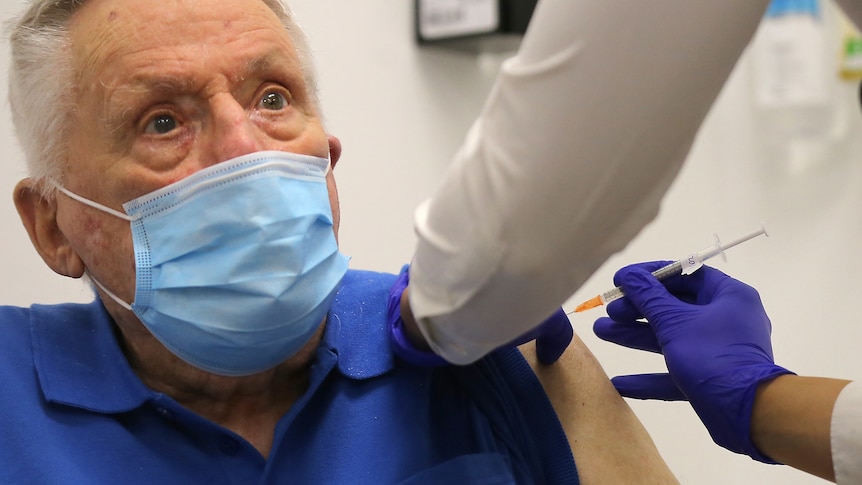 Elderly man in blue shirt, blue mask gets vaccination