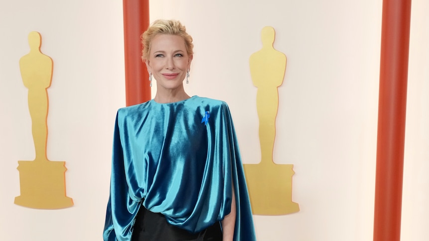 Cate Blanchett wearing a long-sleeved silk blue top with a slim-fitting black skirt with a long train