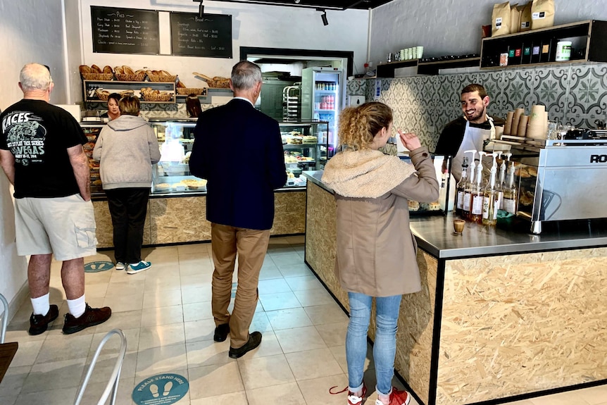 Customers queue in a socially distanced way inside a small bakery shop.