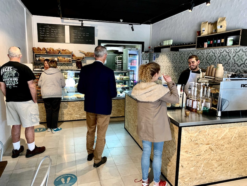 Customers queue in a socially distanced way inside a small bakery shop.