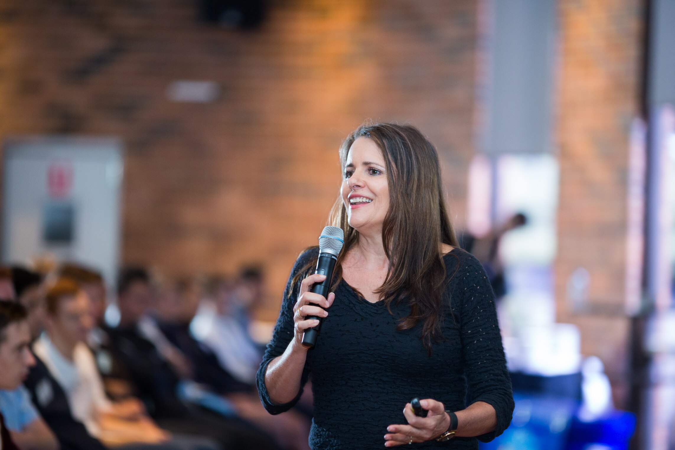 A woman smiles while she speaks into a microphone at an event.