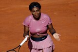 Serena Williams holds her hands out while wearing a pink tennis kit