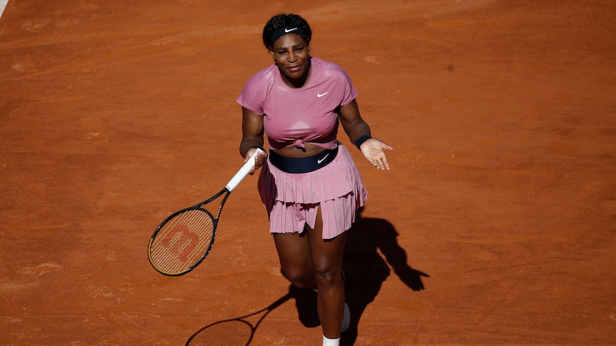 Serena Williams holds her hands out while wearing a pink tennis kit