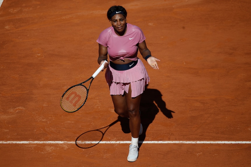 Serena Williams tend les mains en portant un kit de tennis rose