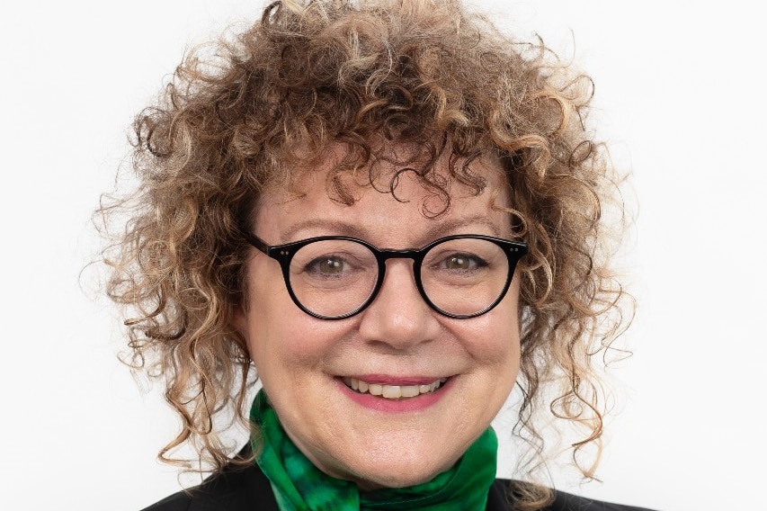A headshot of a woman with curly hair, wearing glasses and a green scarf.