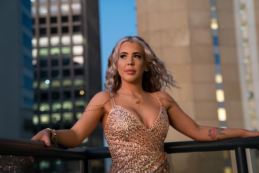 Woman wearing sequin dress, on balcony at dusk.