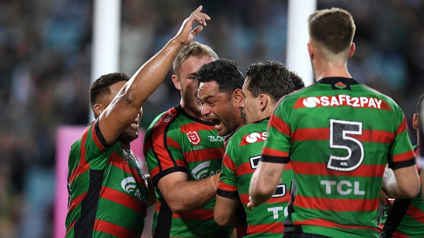 Male NRL players embrace as the celebrate the scoring of a try.