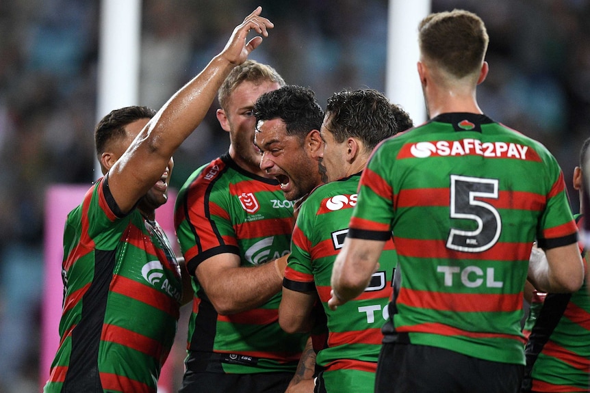 Male NRL players embrace as the celebrate the scoring of a try.