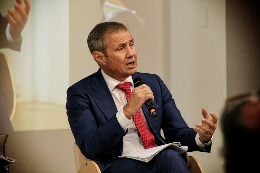 A man in a suit and tie addresses a community forum