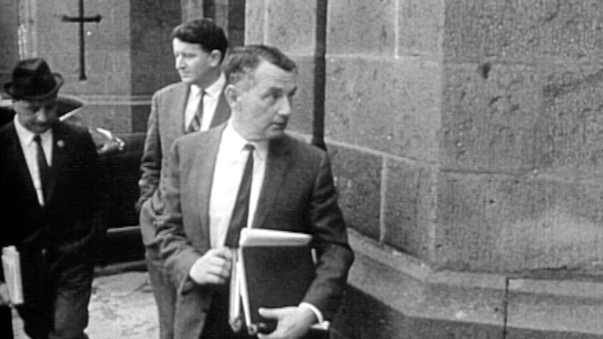 A black-and-white historical image of a lawyer carrying a stack of books walking into a stone courthouse