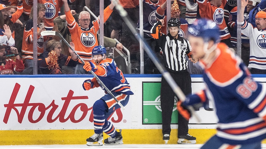 An NHL ice hockey player crouches and punches the air with his fist in celebration as fans cheer after a goal. 