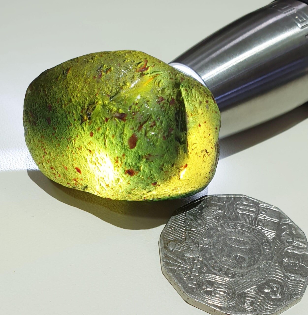 A large yellow rock next to a 50 cent coin. The rock is larger than the coin.