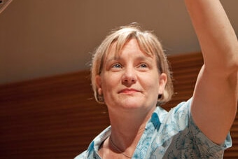 A woman in a blue shirt reaching towards a microphone