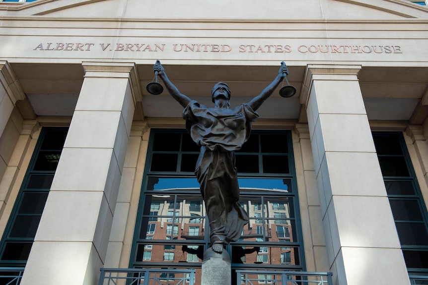 A statue of blind justice with scales is seen outside a large stone United States courthouse.