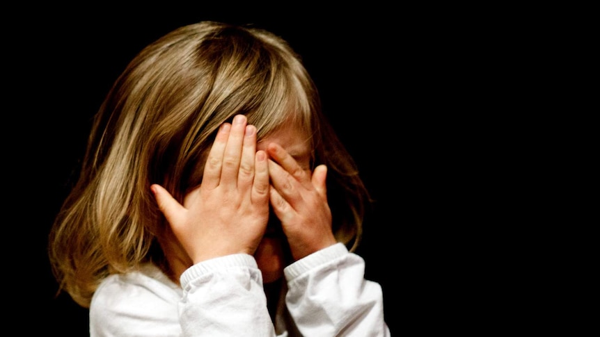 Young girl holding her hands to her eyes.