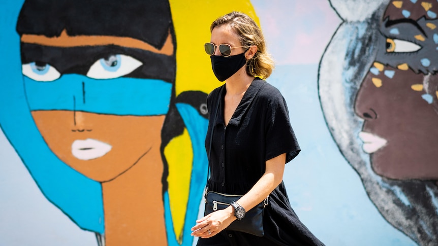 a woman wearing a face mask walking in front of street art