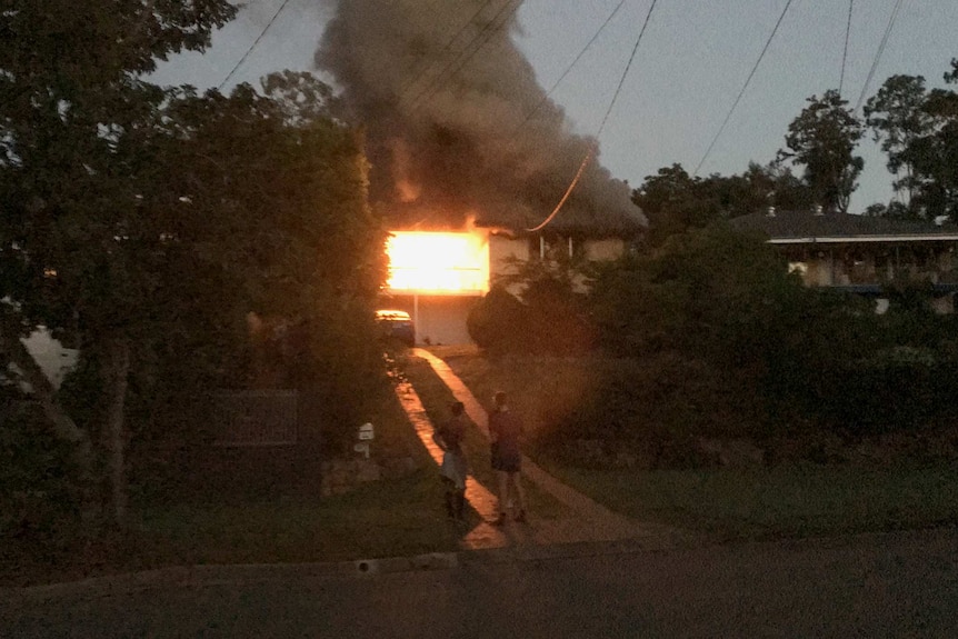 Neighbours stand outside an Everton Hills home fully engulfed in flames, a fire that killed three people.