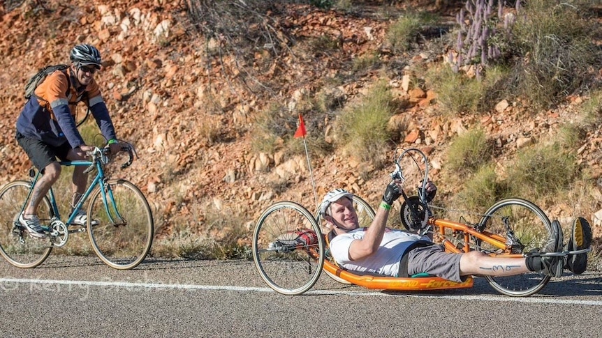 Man on a recumbent bicycle, operating it with hand-driven pedals