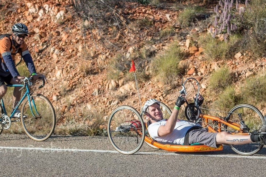 Man on a recumbent bicycle, operating it with hand-driven pedals