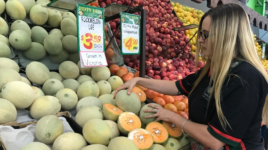 A shop assistant stacks rockmelons in a fruit shop in Wagga Wagga